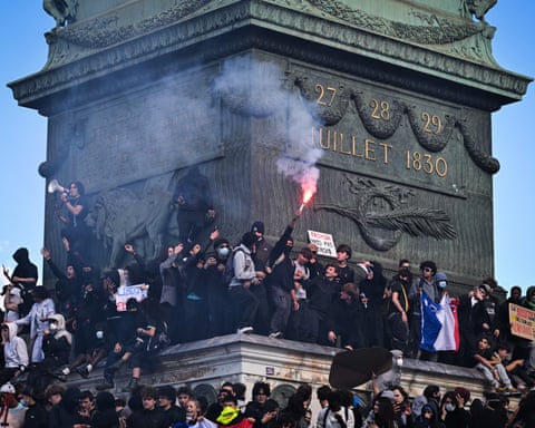Dozens of protesters stand on the plinth of the July Column in Paris, one holding up a lit flare
