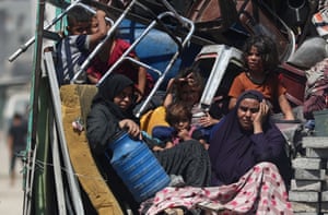 Palestinian women and children sit on a vehicle amid a pile of chairs and a battered mattress after fleeing their homes