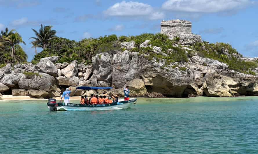 People observe the Pre-Columbian Mayan archaeological site of Tulum from a boat.