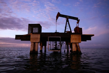 An oil pumpjack stands on a platform above Lake Maracaibo at dusk, silhouetted against a purple sky