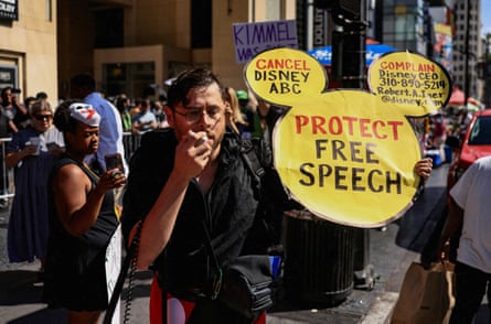 A man holds a Mickey Mouse-shaped sign that says “protect free speech”