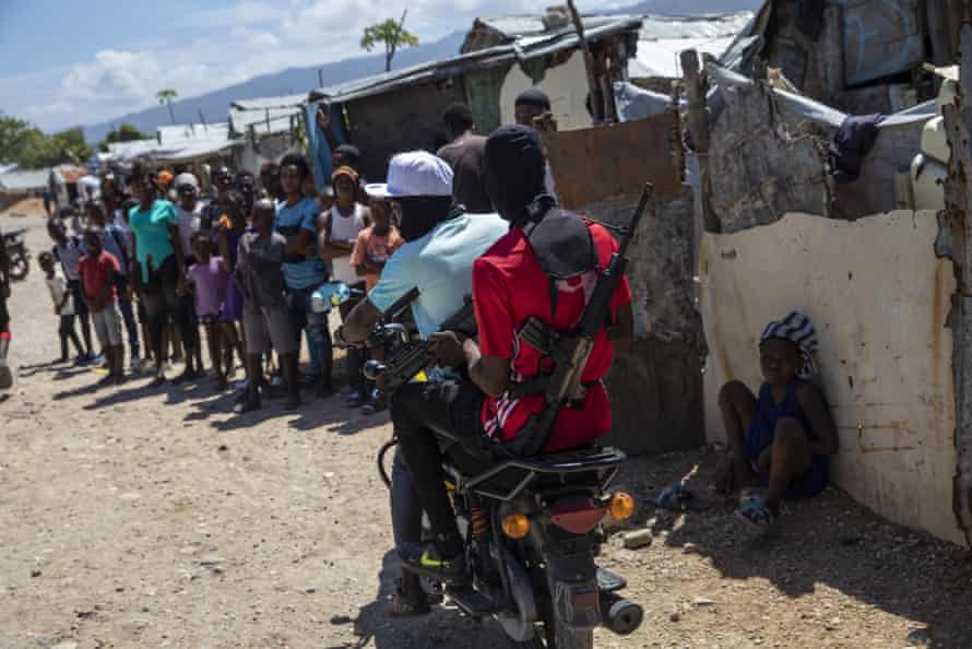 Two men on a motorbike with machine guns drive past onlookers in a market