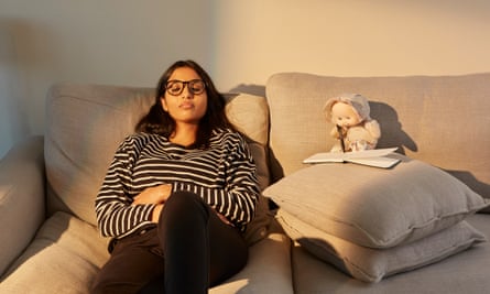 Smriti Benjamin sitting back on a sofa with her eyes shut, with Puffalump propped up on cushions appearing to be holding a pen and writing something
