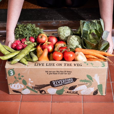 A large vegetable box from Riverford being lifted off a tiled doorstep.