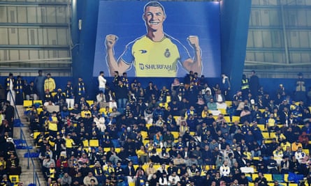 Al Nassr fans sit under a billboard of Cristiano Ronaldo during the Saudi Pro League match between Al Nassr and Al Ettifaq at Mrsool Park Stadium in Riyadh