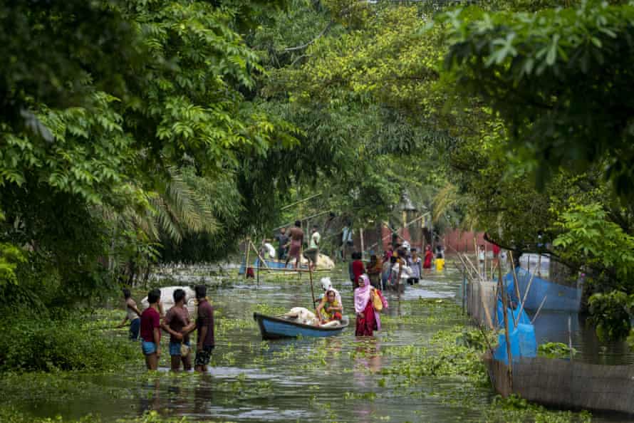 People wade through thigh-high water, some with their possessions in boats.