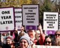 Protesters hold signs reading 'ONE YEAR LATER', 'IMPLEMENT THE SUPREME COURT RULING NOW!' and 'WOMEN WON'T WHEESHT WHILE WE WAIT' at an outdoor rally