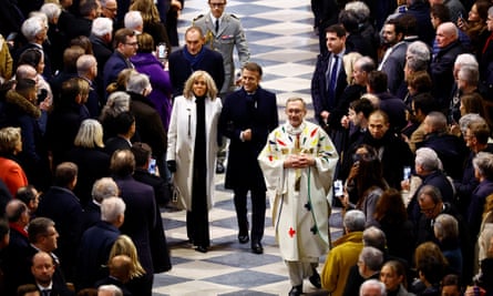 President Macron and Brigitte Macron walk arm in arm up the central aisle of the cathedral, which is packed with people