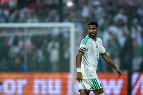 Riyad Mahrez, the Algeria winger and captain, looks over his shoulder while walking to take up a position during a match for his country. He is wearing Algeria’s kit, white with green detailing, and a black captain’s armband.