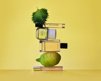 Four bottles of perfume stacked in a pile with a fresh lime and a mint leaf on top.
