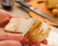 close up of hand spreading peanut butter with knife on bread