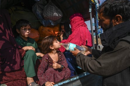 Bir adam küçük bir kıza içmesi için su verirken, iki çocuk ve bir kadın eşyalarıyla birlikte bir kamyonun arka koltuğunda oturuyor 