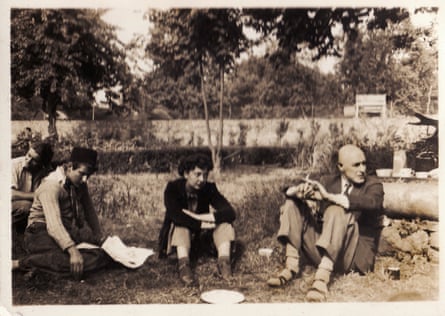 A sepia-toned monochrome photo showing a very young Lucian Freud sitting in a garden with several others; he has his hands on his knees.