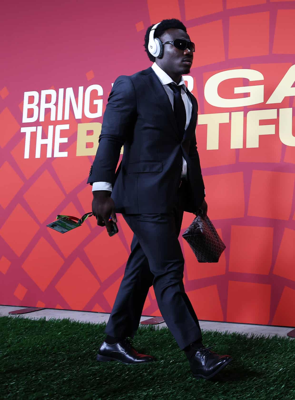 Nestory Irankunda walks in a suit wearing white headphones and clutching a designer bag