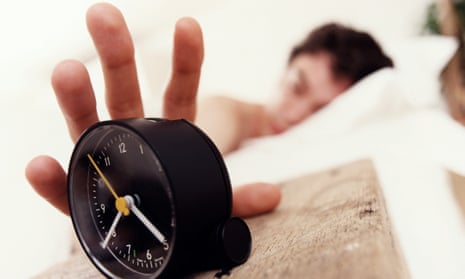 Man in bed reaching for alarm clock