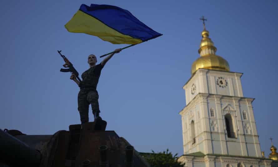 A woman flies the Ukrainian flag on top of a destroyed Russian tank in Kyiv.