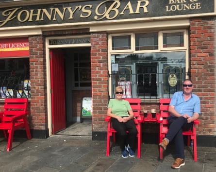 Two people sit on red chairs outside a pub