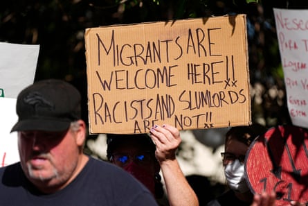 a person holds a sign that says “Migrants are welcome here!! Racists and slumlords are not!!”