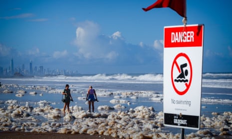 Tourists walk through sea foam at Currumbin beach on Queensland’s Gold Coast