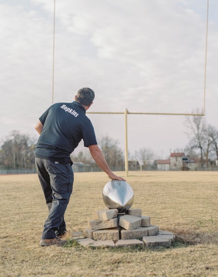 A man in a black shirt with touches a large silver football edifice and looks towards a field goal