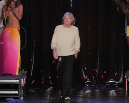 A man in a cream sweater walks on stage