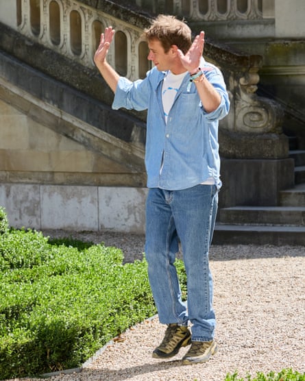 Anderson dressed casusally outside on path with two hands raised