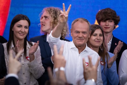 Donald Tusk raises a hand with a V for victory sign as he stands on stage at an election night event