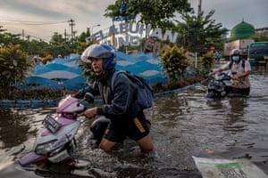 Semarang, Indonesia. Workers push their motorbikes through water at the flooded Tanjung Emas container port terminal area in Central Java province, after high tides and broken seawalls