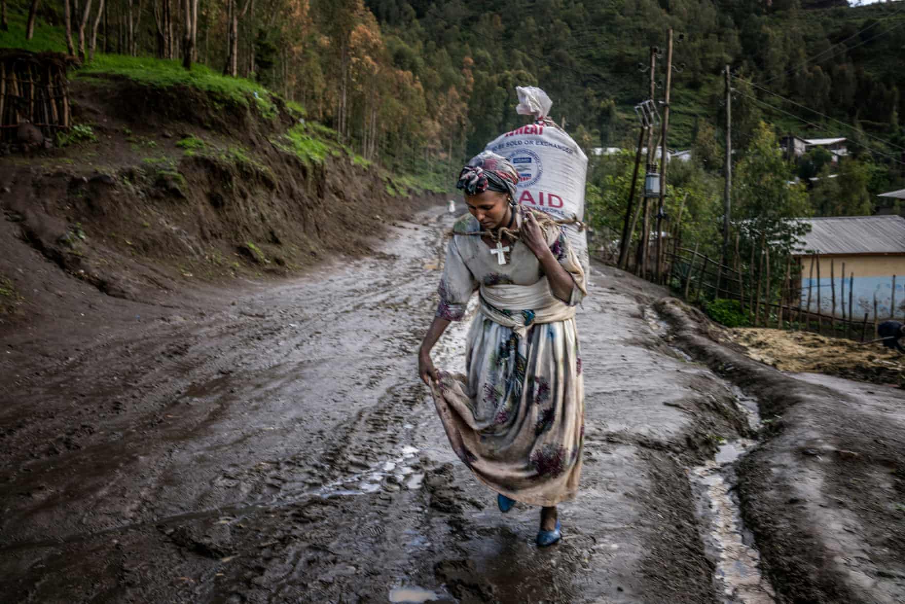 A woman carries a heavy sack of wheat along a saturated road. Unusually heavy summer rains have caused severe flooding, displacing almost 190,000 people via The Guardian