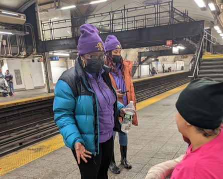 people in purple hats and hoodies talk to person on bench in subway station