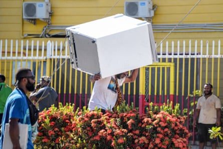 رجل يحمل ثلاجة بينما تغادر الحشود المتاجر بالبضائع المنهوبة وسط حالة من الاضطرابات في بورت مورسبي.