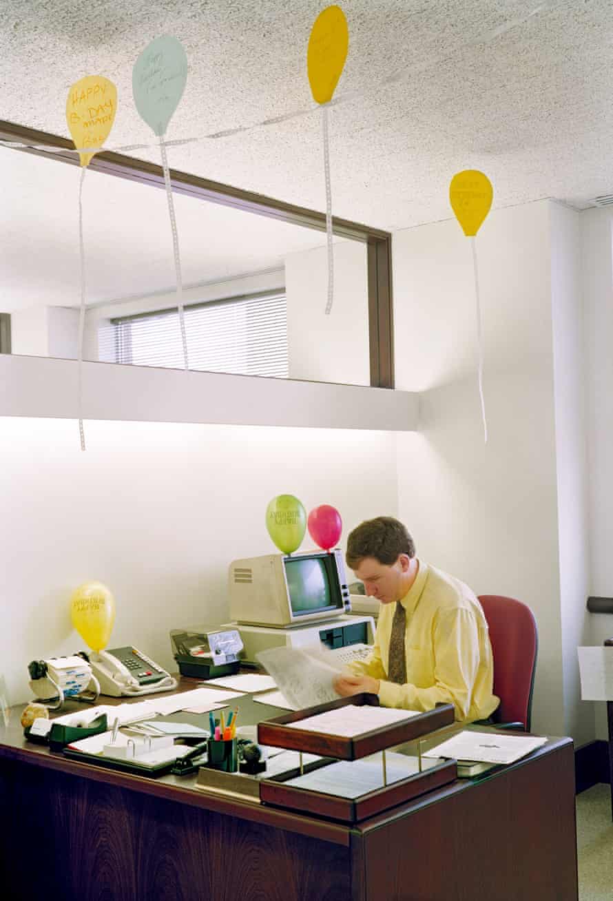 Man sitting at desk with cut out birthday balloons hanging from the ceiling above him