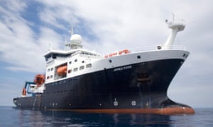 The James Cook, a modern survey vessel with a dark blue hull, photographed from a smaller boat approaching it