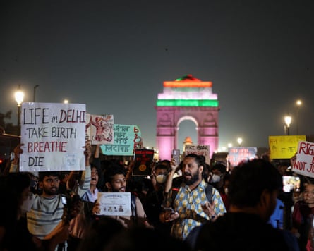 A crowd gathers holding signs that include: 'Life in Delhi - Take Birth, Breathe, Die'