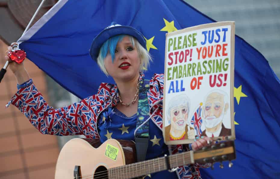 A street musician waves an EU flag and carries a placard saying 'Please just stop! You're embarrassing all of us!' as she performs ahead of a European Council meeting on Brexit, April 2019