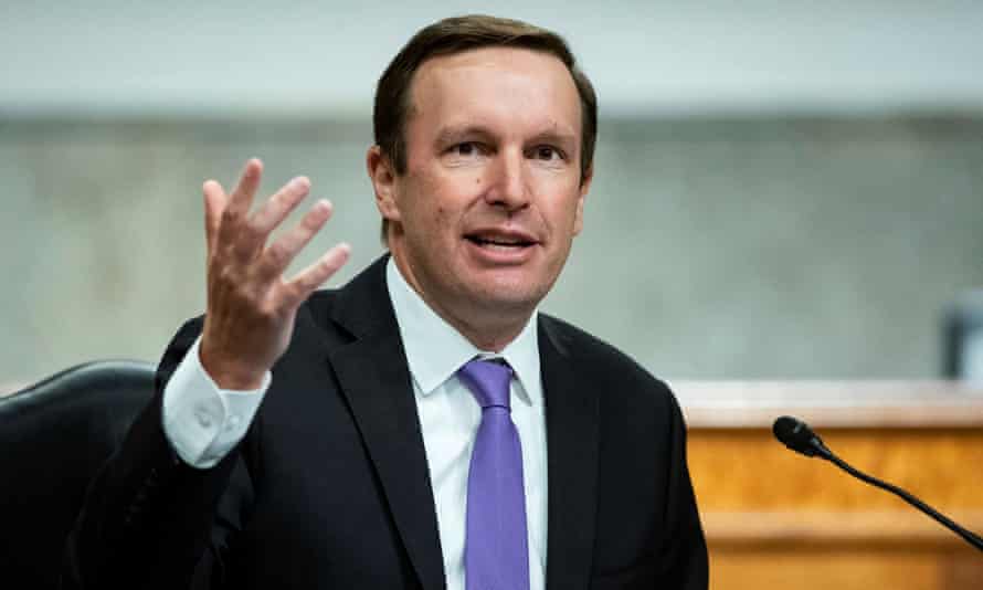 A man wearing a purple tie speaks into a microphone.