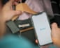 A hand holds a smartphone showing the Vinted app logo near a hanger with clothing