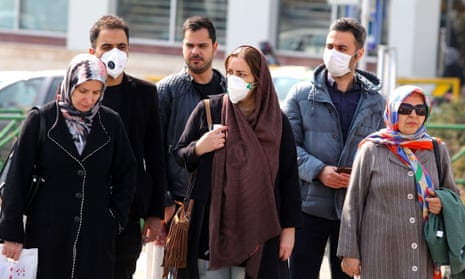 Iranians, some wearing protective masks, wait to cross a street in the capital Tehran