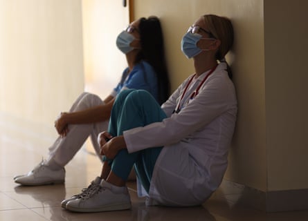 Young female doctor and nurse in medical masks sit in corridor of hospital.
