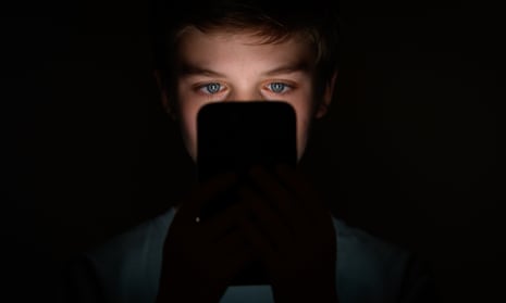 A teenager looks at the screen of a mobile phone in the dark