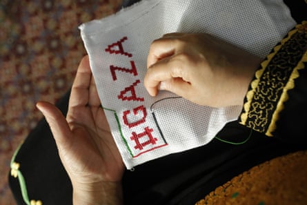A woman’s hands embroider #GAZA on to a piece of white cloth.