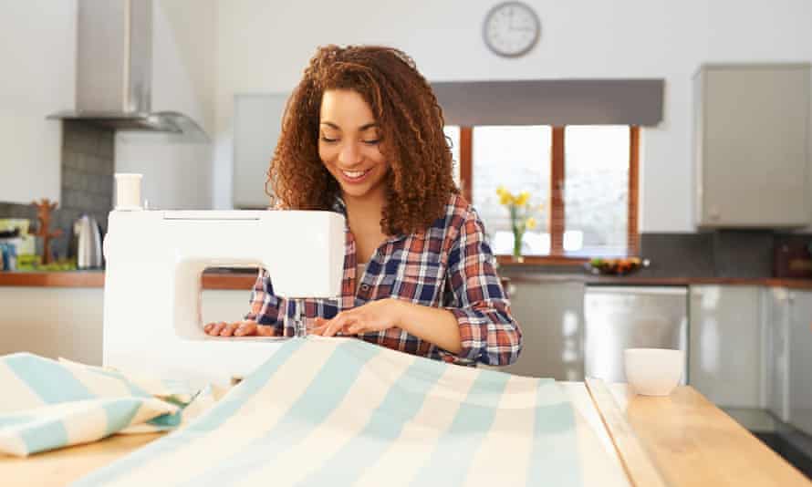Woman at kitchen table using sewing machine. A woman makes curtains at home using a sewing machine.
