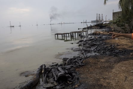 The shore of Lake Maracaibo, which is covered in a film of oil. Offshore drilling terminals can be seen on the horizon.