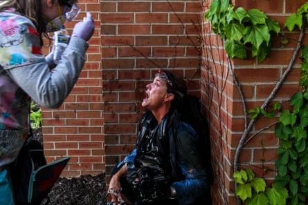Protester has mouth open down near a brick wall while person with gloves on stands near