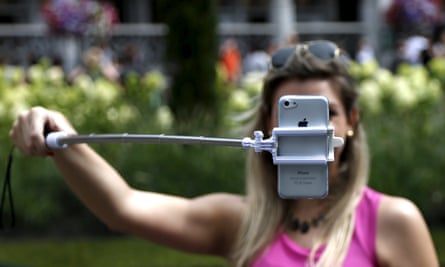 A woman holding a mobile phone on a selfie stick in front of her face