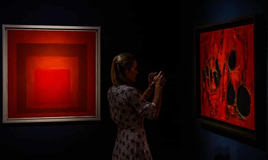 A visitor to Christie’s in London between Homage to the Square: Between 2 Scarlets by Josef Albers and Rosso Plastica by Alberto Burri.
