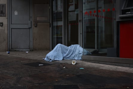 A rough sleeper under a blanket outside a commercial building