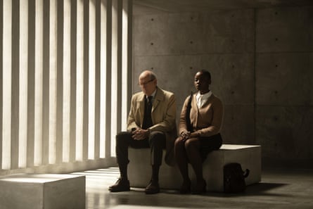 Plumb and Homer look thoughtful as they sit on a stone bench in a darkened room with slight streaming in through vertical columns on their right