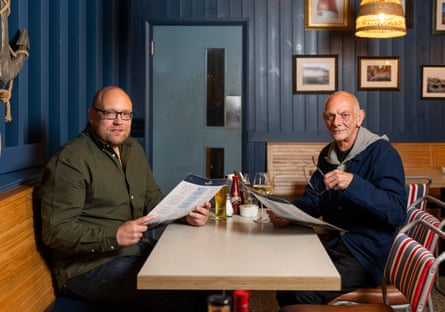 Jonathan and Andrew holding menus and looking at the camera at a restaurant table