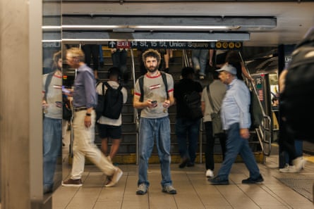 A man in a gray T-shirt stands among commuters on a subway platform.
